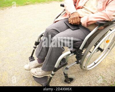 Nahaufnahme des Körpers einer älteren behinderten schwarzen Frau im Rollstuhl, die ihr Telefon auf den Beinen hält Stockfoto