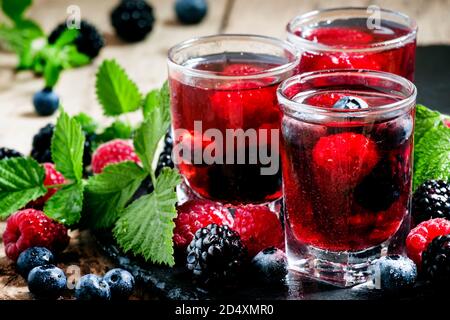 Kalter Sommerbeerentee mit Himbeeren, Heidelbeeren, Brombeeren und Minze in Gläsern auf dunklem Hintergrund, selektiver Fokus Stockfoto