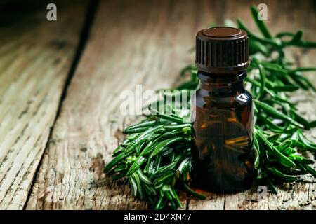 Rosmarin ätherisches Öl in einer kleinen Flasche und frischer Rosmarin auf einem alten Holzhintergrund, selektiver Fokus Stockfoto
