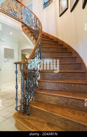 Spiralförmige Holztreppe mit schmiedeeisernem Baluster, die in die obere Etage eines luxuriösen Wohnhauses führt. Stockfoto