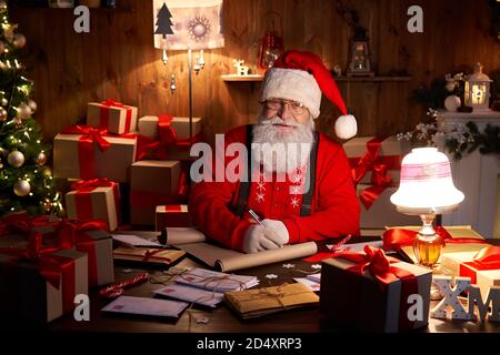 Happy Santa Claus arbeitet an Heiligabend sitzen am heimischen Tisch, Porträt. Stockfoto