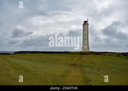 Blick über das Gras an einem bewölkten Tag in Richtung Malarrif Leuchtturm an der Küste im Snaefellsjokull Nationalpark in Westisland. Stockfoto