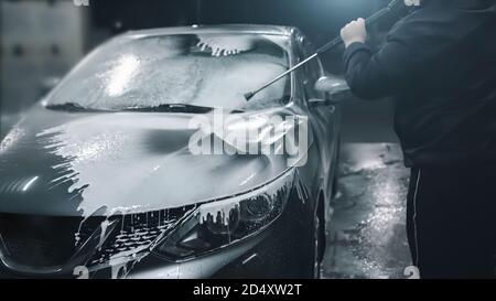 Der Mann wäscht sein Auto bei der Selbstbedienungswaschung, bedeckt das Auto mit Waschschaum. Stockfoto