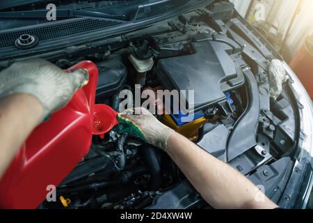 Neues Motoröl aus dem Behälter in den Motortrichter bei der Fahrzeuginservicung aus nächster Nähe gießen. Stockfoto