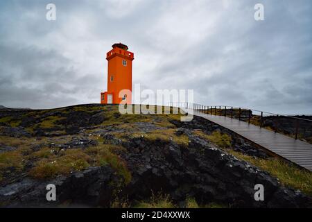 Ein Pfad führt hinauf zum orangefarbenen Leuchtturm Svortuloft auf der Halbinsel Snaefellsnes in Westisland. Der Leuchtturm liegt auf schwarzem Lavastein. Stockfoto