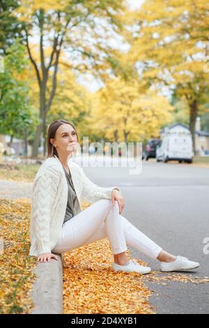 Schöne mittlere Alter kaukasischen Frau mit kurzen Haaren sitzen im Herbst Straße im Freien. Junge Frau mit kurzen Haarschnitt in Freizeitkleidung im Park o Stockfoto