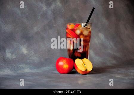 Ein hohes Glas roter Sokas mit Eis und Stroh, daneben zwei reife rote Äpfel auf grauem Grund. Nahaufnahme. Stockfoto