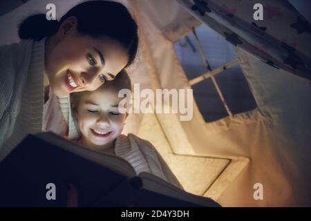 Familie Schlafenszeit. Mutter und Kind Tochter lesen ein Buch im Zelt. Ziemlich junge Mutter und schönes Mädchen mit Spaß im Kinderzimmer. Stockfoto