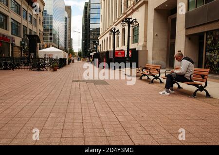 Ottawa, Ontario, Kanada - 8. Oktober 2020: Ein Mann benutzt ein Smartphone auf einer Bank, einer von wenigen Menschen in der Sparks Street Mall. Der Platz im Freien hat gesehen Stockfoto