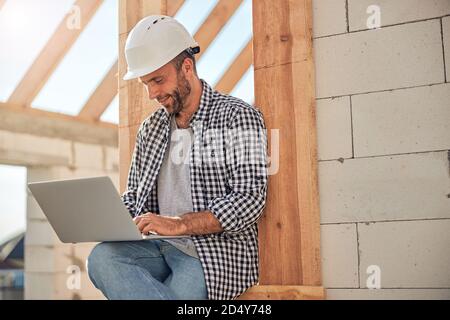 Ambitionierter Außendienstingenieur, der in der Nähe eines Gebäudes an seinem Laptop arbeitet Stockfoto