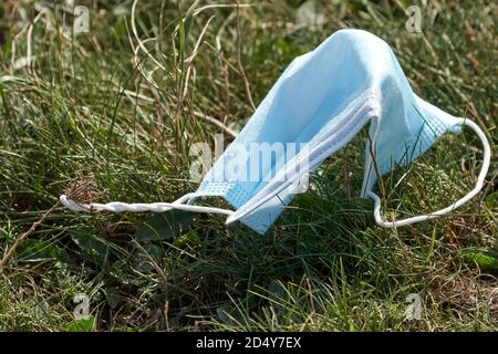 Gebrauchte blaue Gesichtsmaske auf dem Boden im Gras. Gesichtsmaske ist falsch entsorgt. Umweltverschmutzung und Umweltkatastrophe. Covid-19 Pandemie Stockfoto