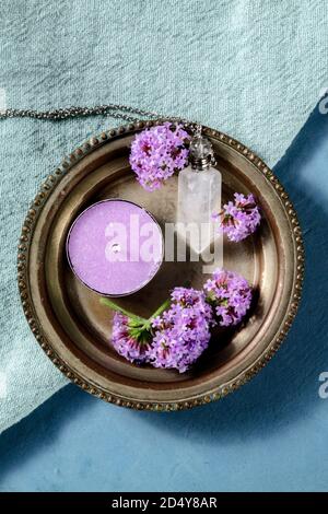 Verbena Blumen, Kerze, und ein Kristall Fläschchen für ätherische Öle, über Kopf auf einem blauen Hintergrund geschossen Stockfoto