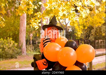 Ein Kind in einem Faschingskostüm an Halloween mit großen farbigen Luftballons. Halloween für Kinder. Kleines Mädchen im Herbstpark. Der Fokus wird auf dem Hauptobjekt sanft verschoben. Speicherplatz kopieren. Stockfoto