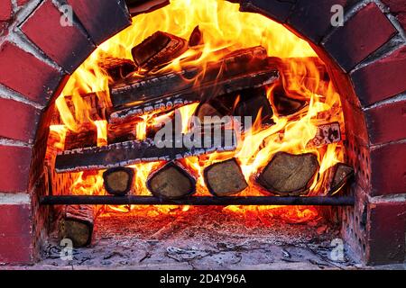Traditioneller Backsteinofen im Freien mit brennendem Holz im Inneren. Kochen im Landhaus Stockfoto