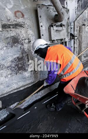 Asiatische Arbeitskräfte mit Schaufel reinigen Abwasser in der Kanalisation in der Zementfabrik. Harte Arbeit Konzept. Stockfoto
