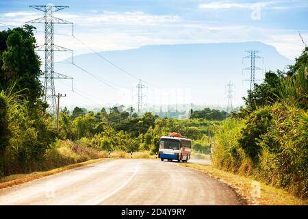 Ein lokaler Bus, der auf der Bergstraße des Bolaven-Plateaus, Süd-Laos, in Richtung der Stadt bei Laos und Vietnam-Grenze, Berge im Hintergrund, fährt. Stockfoto