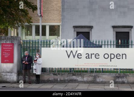 Ein Paar wartet während der Coronavirus-Krise im Oktober 2020 neben dem Poster "We are open" im Fitzwilliam Museum, Cambridge University, England. Stockfoto