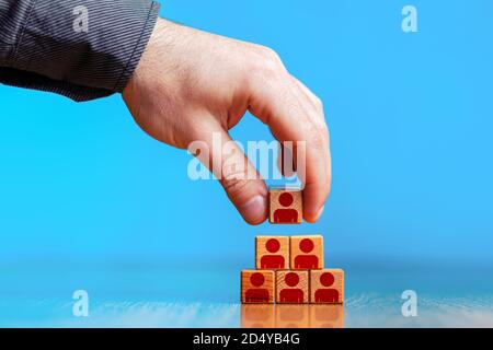 Geschäftskonzept Personalmanagement und Personalbeschaffung. Hand setzen Holz Würfel Block auf der obersten Pyramide. Speicherplatz kopieren. Blauer Hintergrund. Stockfoto