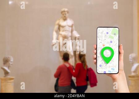 Eine weibliche Hand hält ein Smartphone mit einer Online-Karte auf dem Bildschirm. Im Hintergrund schauen ein paar Leute die Statue unscharf an. Concep Stockfoto