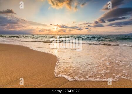 Eine Sunset Ocean Wave bricht an der Küste mit der Sonne am Ocean Horizon Stockfoto