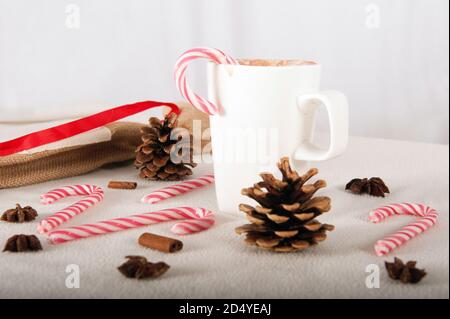 Weiße Tasse heiße Schokolade mit Zuckerrohr. Rotes Band und Pinecones auf dem Tisch. Stockfoto
