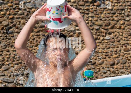 Ein kleiner Junge gießt kaltes Wasser über seinen Kopf zu Cool Stockfoto