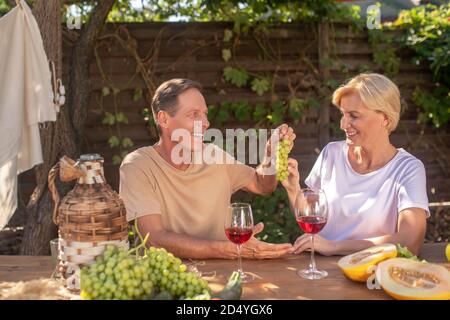 Ein Paar mittleren Alters sitzt draußen am Tisch und genießt die Trauben Stockfoto