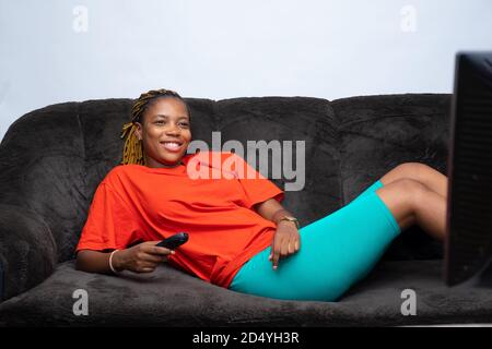 Schöne afrikanische Dame liegt auf einer Couch und schaut Fernsehen Stockfoto