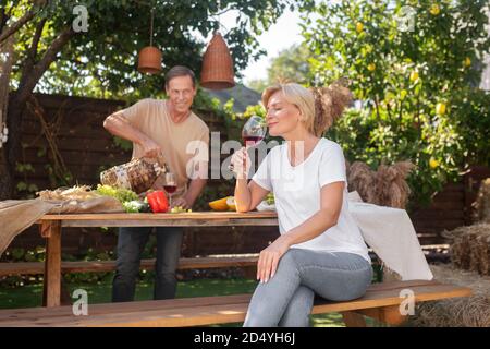 Mann gießt Wein in Glas, blonde Frau genießt Rotwein Stockfoto