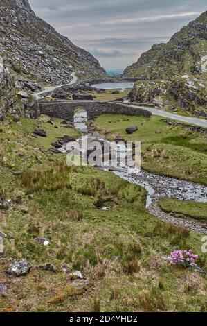 Kleine Straße schlängelt sich durch die Lücke von dunloe, Irland. Panoramablick auf die Gap of Dunloe, Irland. Kleiner Bach fließt durch die Gap of Dunloe in I Stockfoto