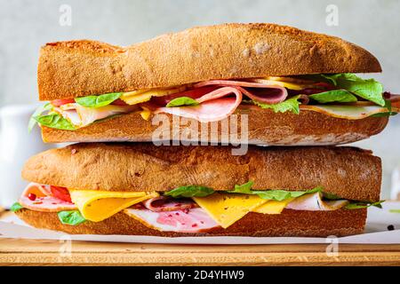 Baguette-Sandwich mit Fleisch, Käse und Gemüse auf einem Holzbrett. Stockfoto