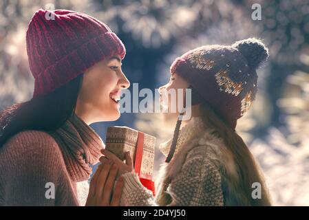 Frohe Weihnachten und schöne Feiertage! Fröhliche Mutter und ihre nette Tochter Mädchen Austausch von Geschenken. Eltern und kleine Kinder haben Spaß im Freien. Liebende Familie Stockfoto