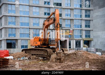 Orange Bagger am Gebäude im Bau. Сonstruction Fahrzeug verwendet, um zu graben oder bewegen objectsю. Bagger gräbt den Boden für das Fundat Stockfoto