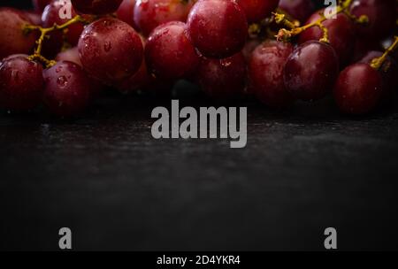 Rote Trauben mit Wassertropfen auf schwarzem Hintergrund - Fotografie von dunklen Speisen Stockfoto
