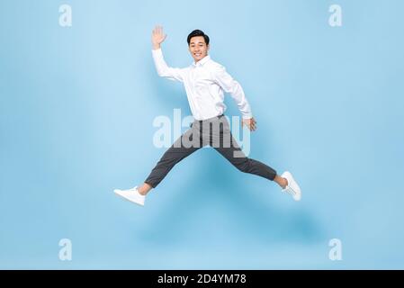 In voller Länge Porträt von glücklich lächelnd energisch asiatischen Mann in Halbformelle Kleidung springt in der Luft isoliert auf Licht Blauer Hintergrund Stockfoto