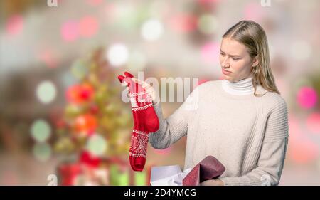 Ein enttäuschendes Weihnachtsgeschenk für eine junge Frau davor Von verschwommenem weihnachtshintergrund Stockfoto