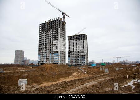 Turmdrehkrane arbeiten auf der Baustelle gegen grauen Himmel. Verlegung von Betonschächten und Abflussrohren für das Regenwassersystem. Bau Regenwasser und U Stockfoto