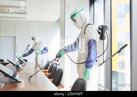 Seitenansicht Porträt von zwei Arbeitern in Gefahrgutanzügen Desinfektion Konferenzraum im Büro, Kopierraum Stockfoto