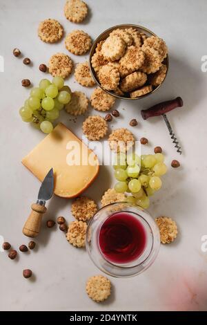 Wein Snack. Käse, Trauben, Nüsse, Käse, Cracker Kekse mit Glas Rotwein und Messer über weißem Marmor Hintergrund. Flach, Raum Stockfoto