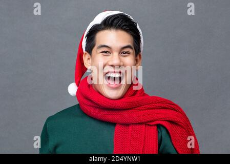 Glücklich überrascht schöner asiatischer Mann trägt bunte rot und grün Weihnachtskleidung im Studio grauen Hintergrund Stockfoto