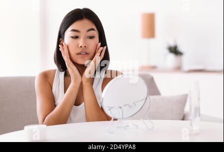 Junge asiatische Frau massiert ihr Gesicht suchen in den Spiegel Stockfoto