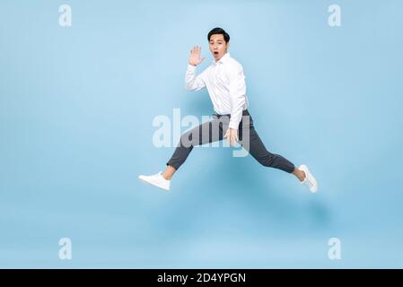 Spaß energetische asiatische Mann in semi formale Kleidung springen in Mittlere Lufteinstrahlung auf hellblauem Hintergrund isoliert Stockfoto