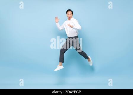Energetische asiatische Mann in semi formale Kleidung springen in der Mitte Luft auf hellblauem Hintergrund isoliert Stockfoto