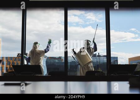 Weitwinkel-Rückansicht Porträt von zwei Arbeitern tragen Gefahrgut Anzüge Desinfektion Fenster im Bürogebäude stehen gegen blauen Himmel, Kopierer Raum Stockfoto