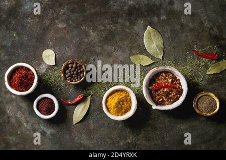 Gewürze Gewürze und Kräuter Vielfalt in Keramik Schalen. Verschiedene Paprika, Chili, Kurkuma, Lorbeer, Zimt über Dark Metal Hintergrund. Stockfoto