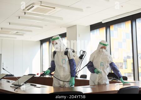 Weitwinkel-Porträt von zwei Sanitäter tragen Gefahrgut Anzüge Reinigung und Desinfektion Konferenzraum im Büro, Kopierer Raum Stockfoto