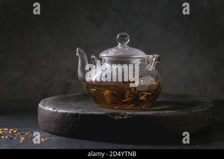 Hot grüner Tee in transparenten Glas Teekanne stehen auf Lehm Fach über schwarzem Marmor tisch. Stockfoto