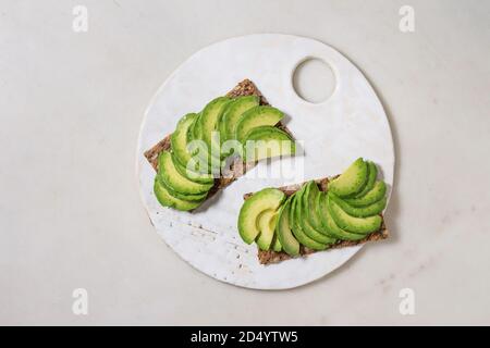 Veganen Sandwiches mit in Scheiben geschnittenen Avocado auf Roggenbrot serviert auf Keramik Brett über weißem Marmor Hintergrund. Flach, Raum Stockfoto