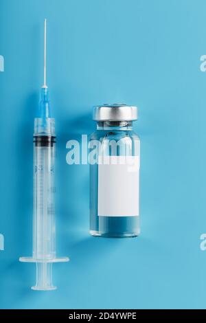 Spritze und Ampulle mit einem Impfstoff gegen Viren und Krankheiten auf blauem Hintergrund. Freier Platz auf dem Ampullen-Etikett für Text, vertikaler Rahmen Stockfoto