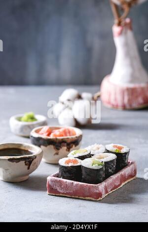 Sushi Rollen in rosa Keramik Servierteller mit Schalen aus Sojasoße und Essig eingelegte Ingwer, Baumwolle Blumen auf hellblau Tabelle. Japan Menü Stockfoto